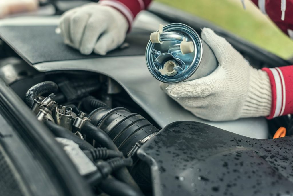Technician servicing fuel system components under the hood of a vehicle